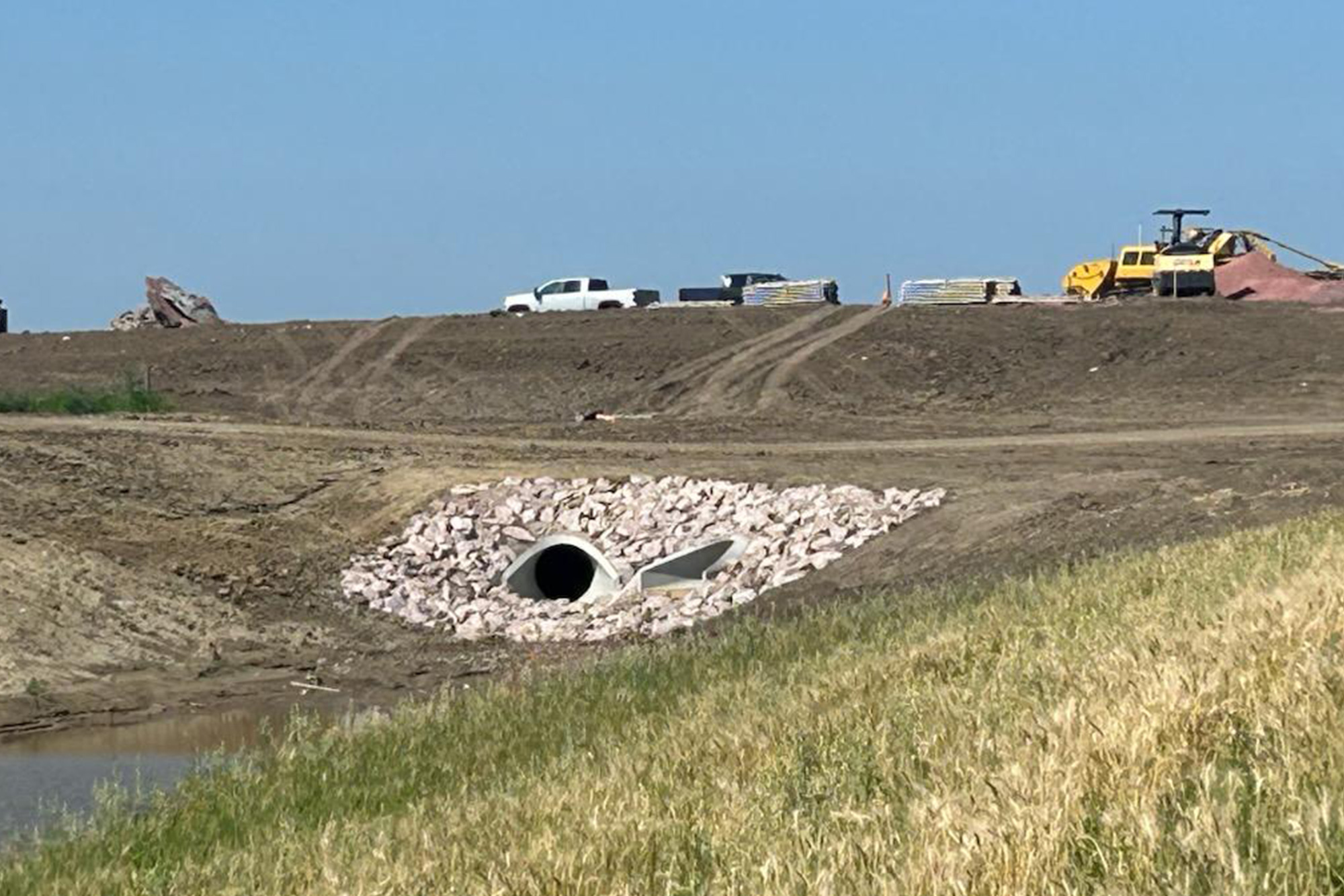 New drainage culvert conduit and rocks around it, leading into a wet swale.