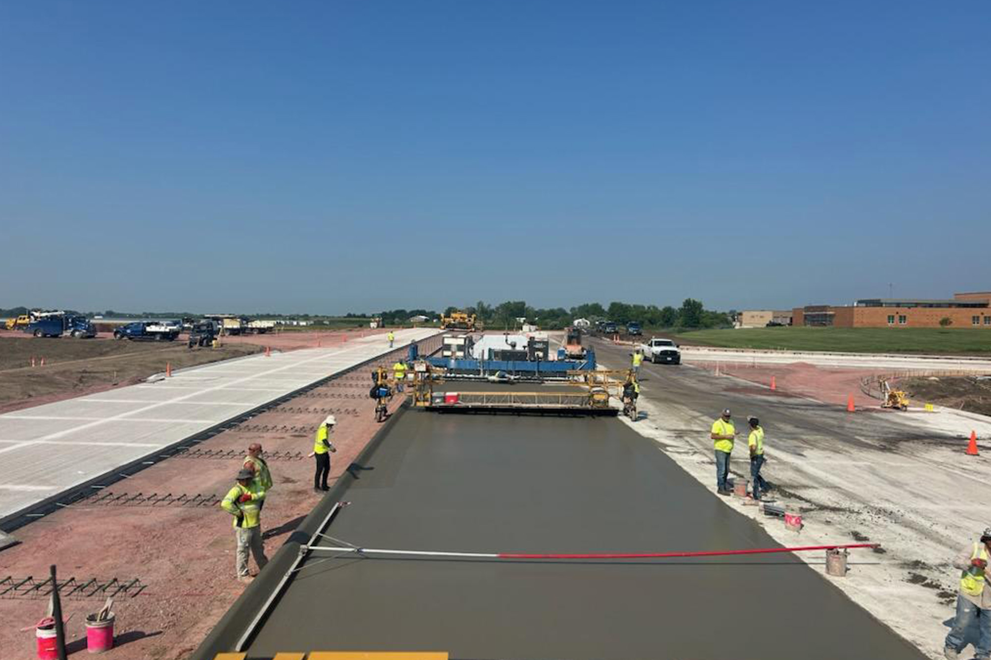 Construction workers leveling freshly poured concrete on new roadway surface.